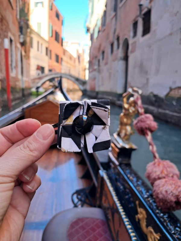 Pince à cheveux en origamie en forme de fleur elle est noi et blanche et est mis sur une gondole a venise